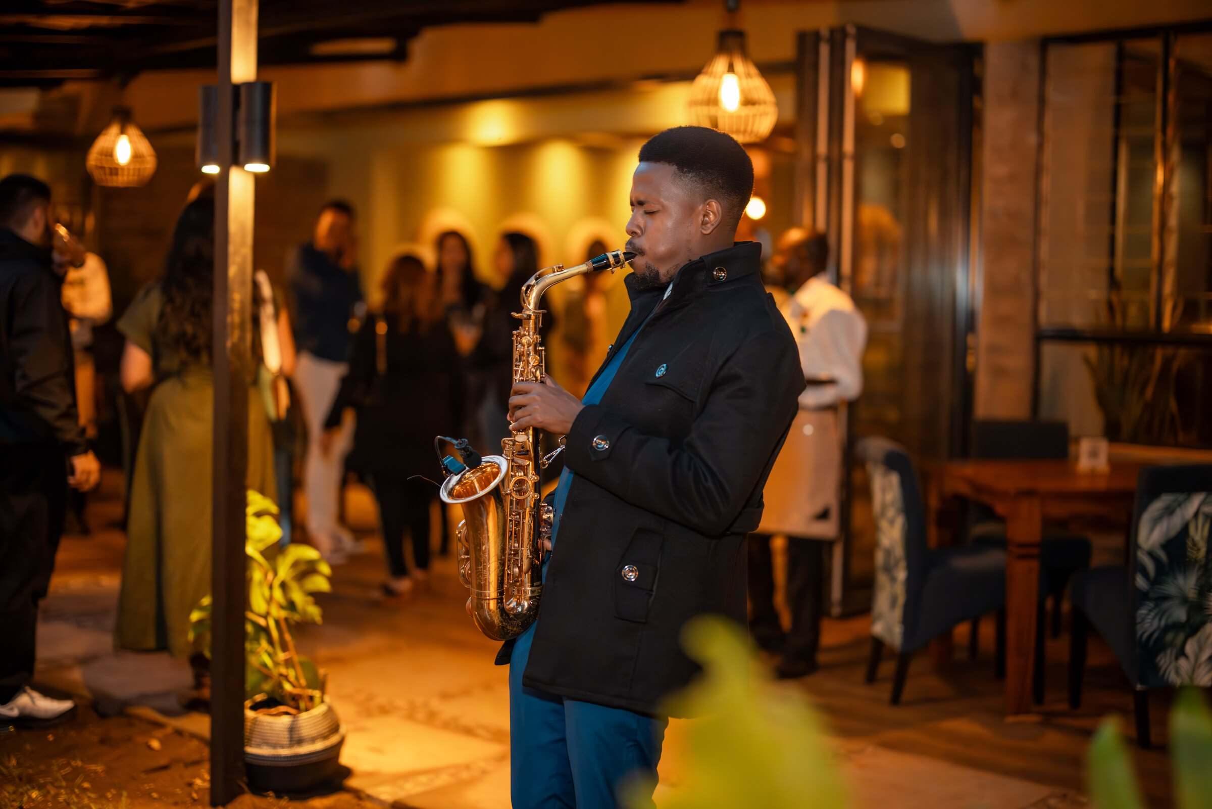 Ian playing saxophone among guests on a warmly lit terrace at an evening reception