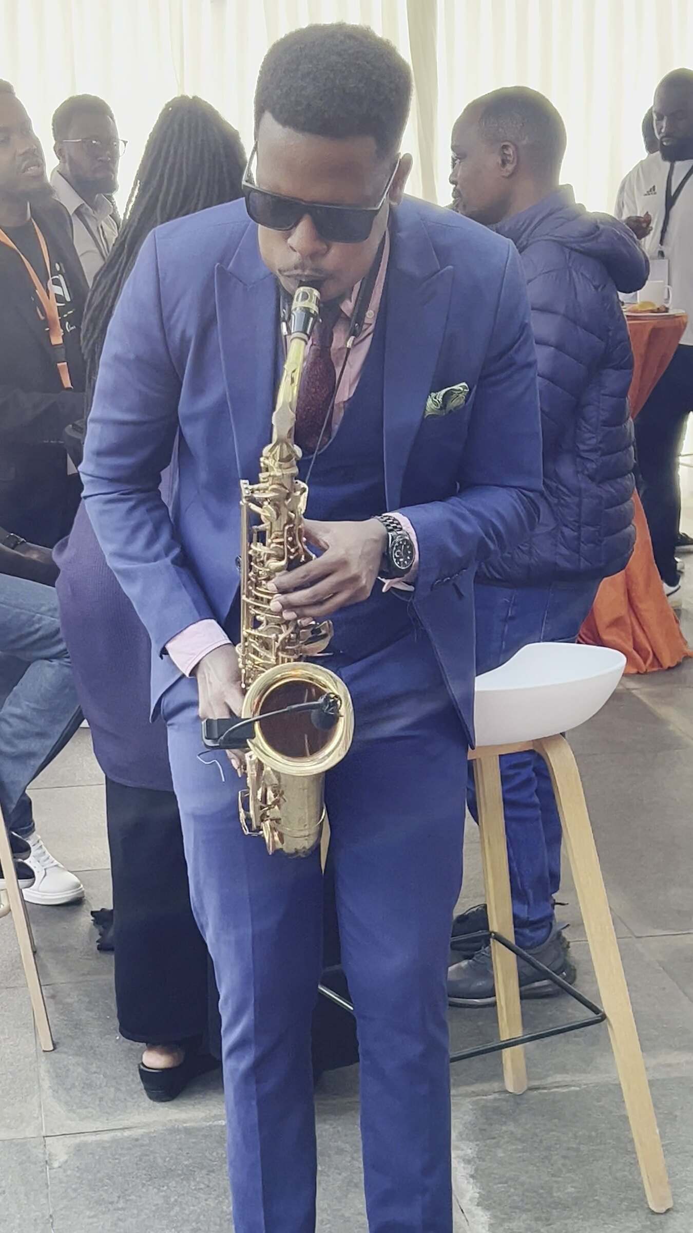 Ian in a blue suit walking among guests under a marquee while playing saxophone